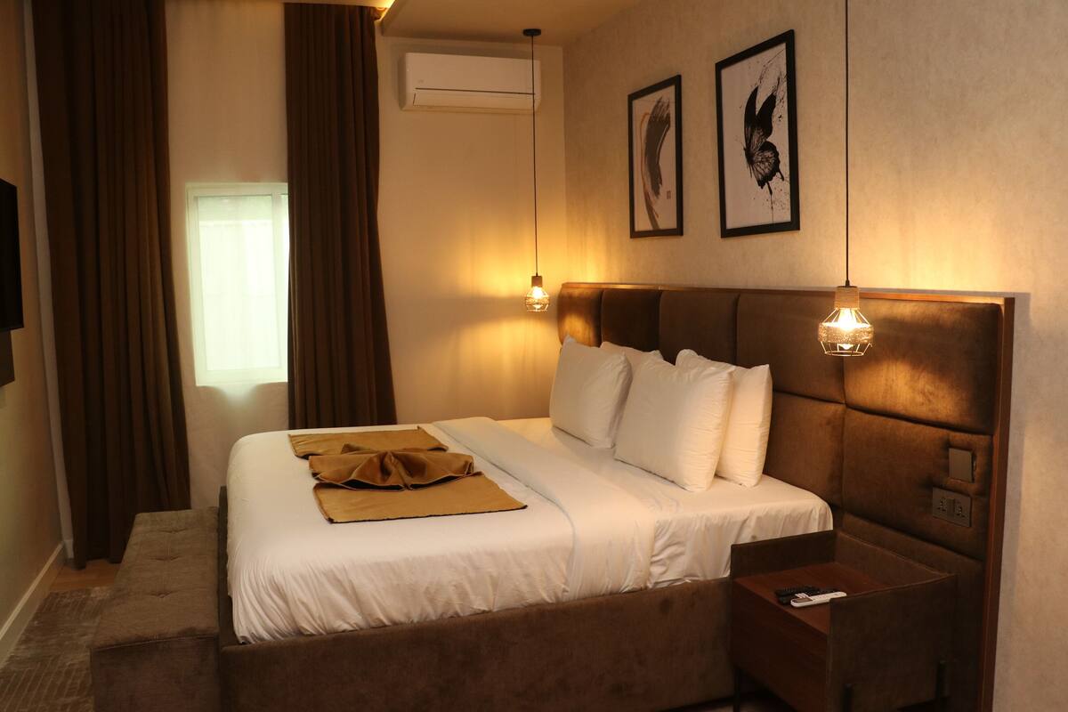 Habitación de hotel con una cama grande, una mesita de noche, aire acondicionado montado en la pared y dos lámparas de pared.