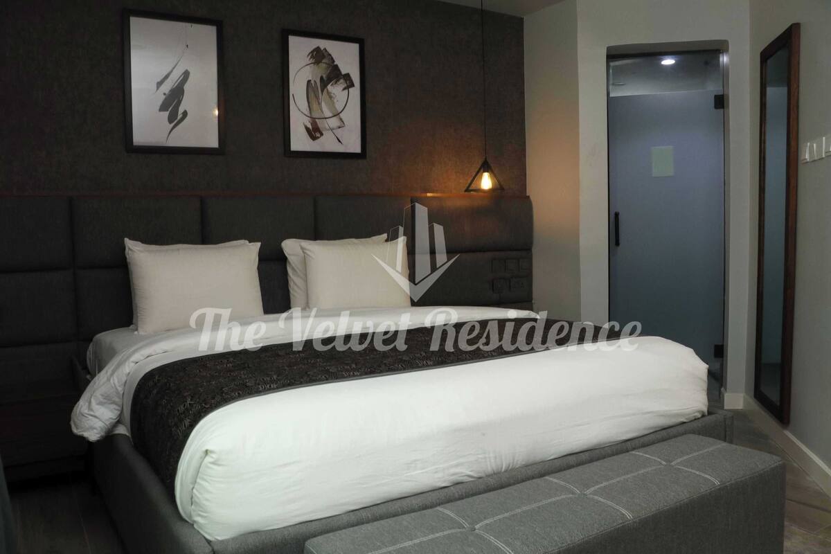 Un dormitorio moderno con una cama grande, cabecera y mesita de noche. Hay dos cuadros enmarcados en la pared sobre la cama.
