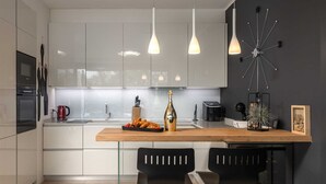 A modern kitchen with white cabinets, a wooden countertop, two black barstools, and pendant lighting.