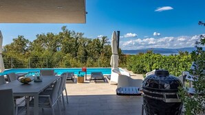 A poolside area with a table, chairs, and a grill.