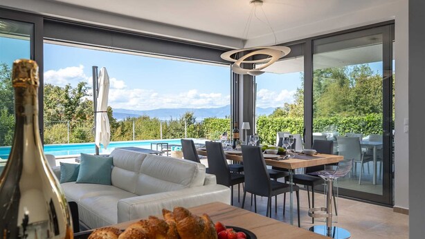 A modern dining area with a pool view, a wooden table, and a bottle of champagne.