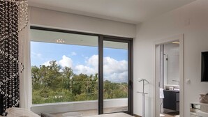 A modern bedroom with a large sliding glass door leading to a balcony, a bed with a view, and a walk-in closet.