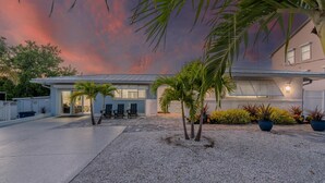 A modern house with a covered patio, outdoor seating, and a gravel driveway. - Miramar Palms (Fort Myers Beach)
