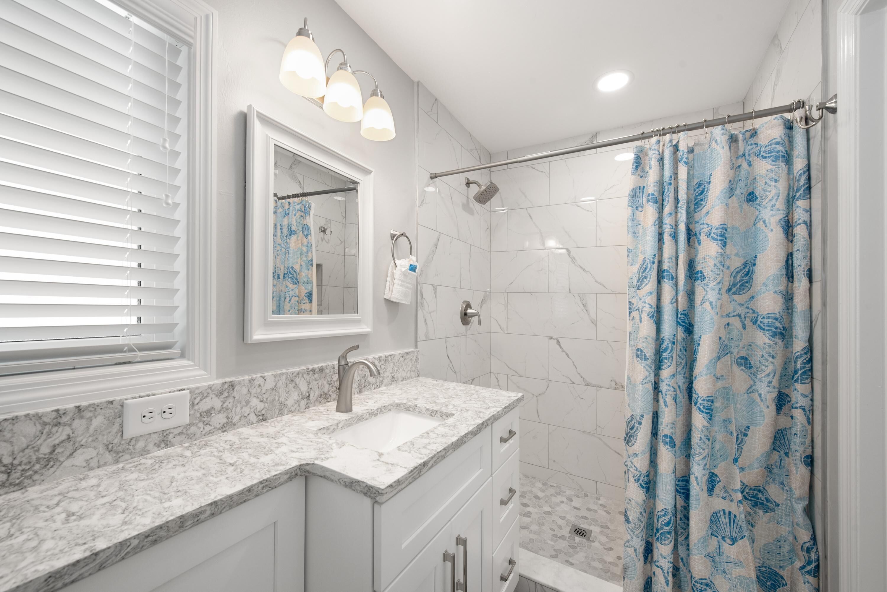 Un baño con tocador blanco, ducha con puerta de cristal y cortina de baño azul.