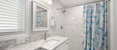 Un baño con tocador blanco, ducha con puerta de cristal y cortina de baño azul.