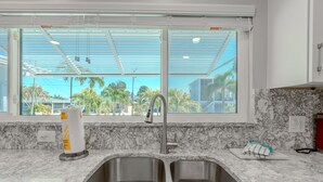 A kitchen with a double sink, a window with a view of palm trees, and a marble countertop. - Miramar Palms (Fort Myers Beach)