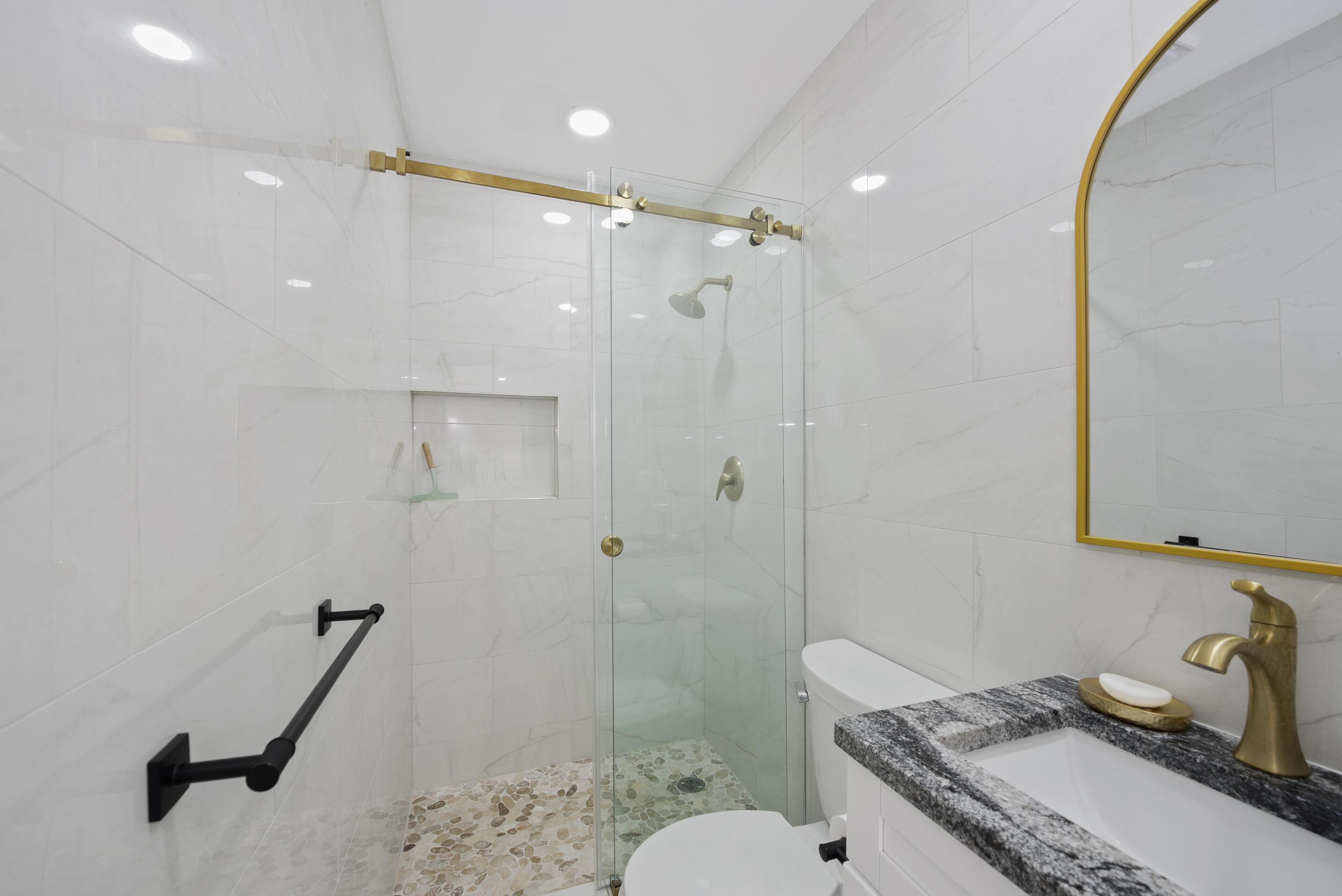 Een moderne badkamer met een douchekabinet van glas, een marmeren wastafel en een goudkleurige kraan.