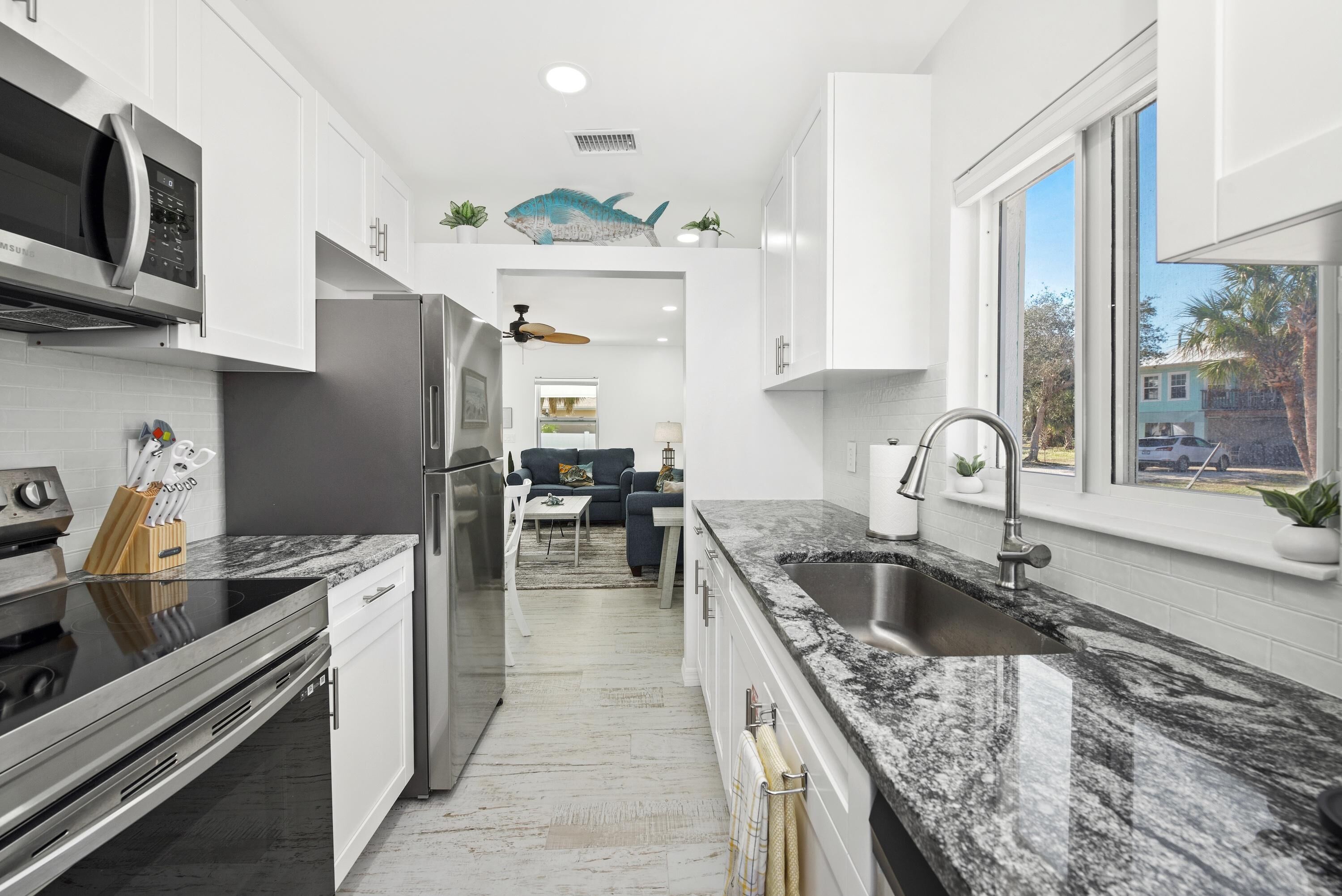 A modern kitchen with white cabinets, a stainless steel refrigerator, a granite countertop, and a large window.