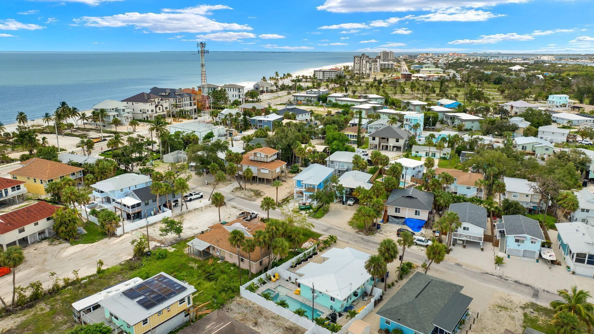 Vue aérienne d’un quartier résidentiel situé sur la côte, avec des maisons, une plage et, au loin, la silhouette d’une ville.
