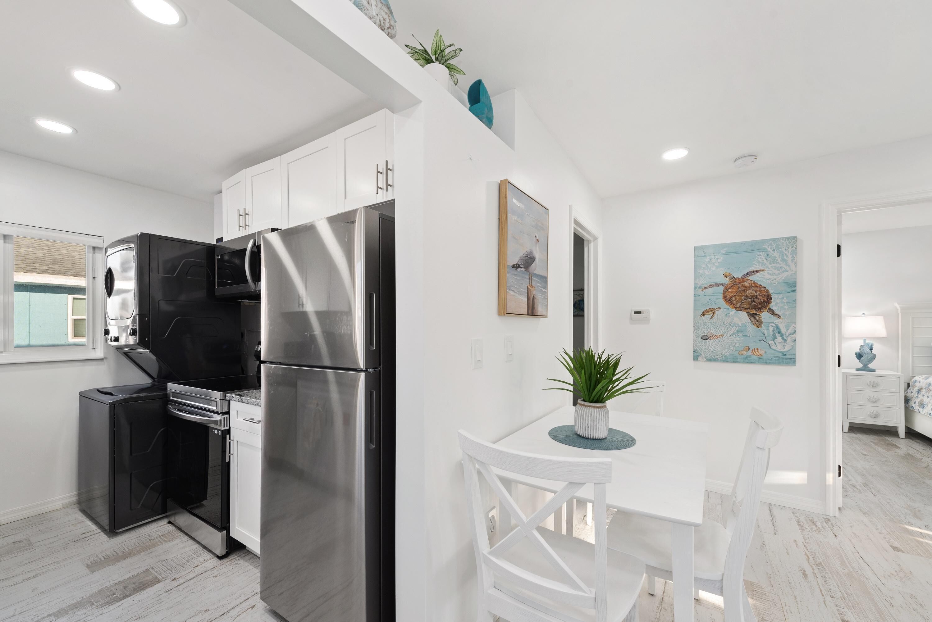 A modern kitchen with stainless steel appliances, white cabinetry, and a dining area with a white table and chairs.