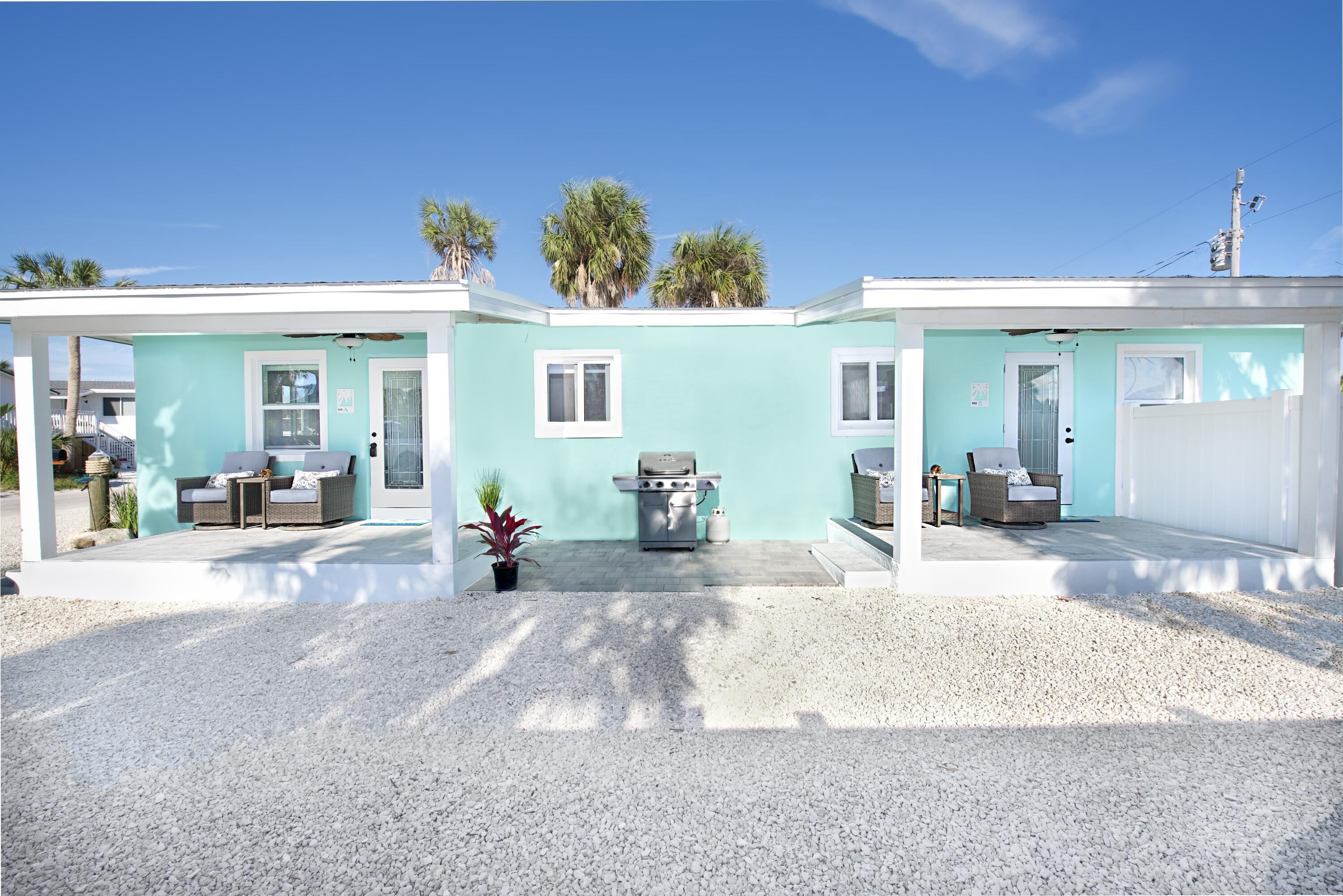 A two-story building with a light blue exterior, a patio area with outdoor furniture, and a grill.