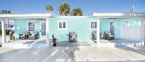 A two-story building with a light blue exterior, a patio area with outdoor furniture, and a grill.