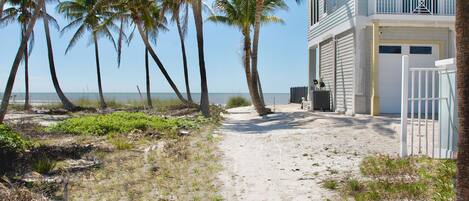 A beachfront property with a sandy path leading to a white building with a balcony.