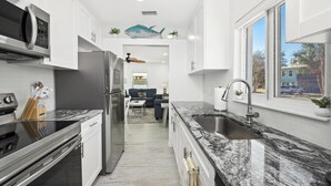 A modern kitchen with white cabinets, a stainless steel refrigerator, a granite countertop, and a large window. - Coconut Villa A (Fort Myers Beach)