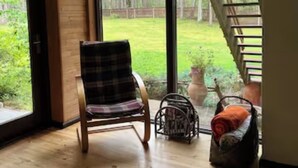 Une pièce avec un plancher en bois, un fauteuil à carreaux, un panier en osier et un escalier menant à l’extérieur.