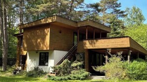 Une maison en bois à deux étages, dotée d’un porche abrité, entourée d’une pelouse bien entretenue et d’arbres.