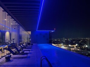A rooftop pool area with lounge chairs and a city view at night.
