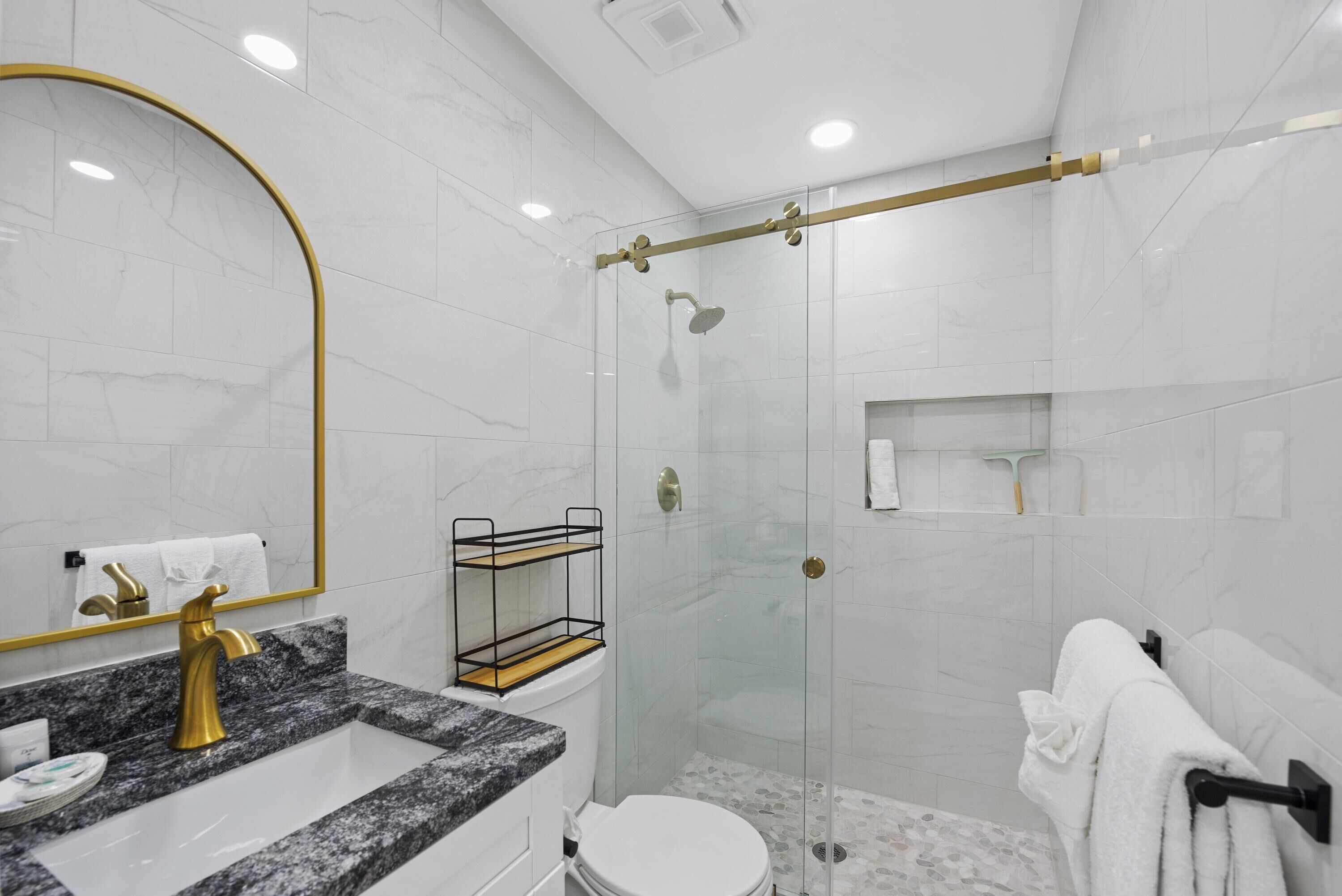 Une salle de bain moderne avec un lavabo en marbre, des robinetteries dorées, une douche en verre et des toilettes blanches.