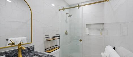Une salle de bain moderne avec un lavabo en marbre, des robinetteries dorées, une douche en verre et des toilettes blanches.