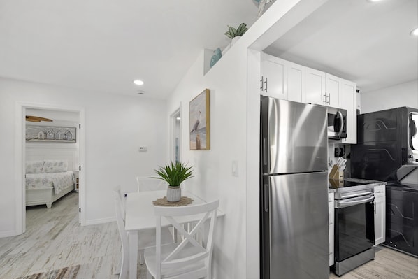 Enjoy a compact kitchenette with a refrigerator and oven, a dining area with a table and chair, and a potted plant.