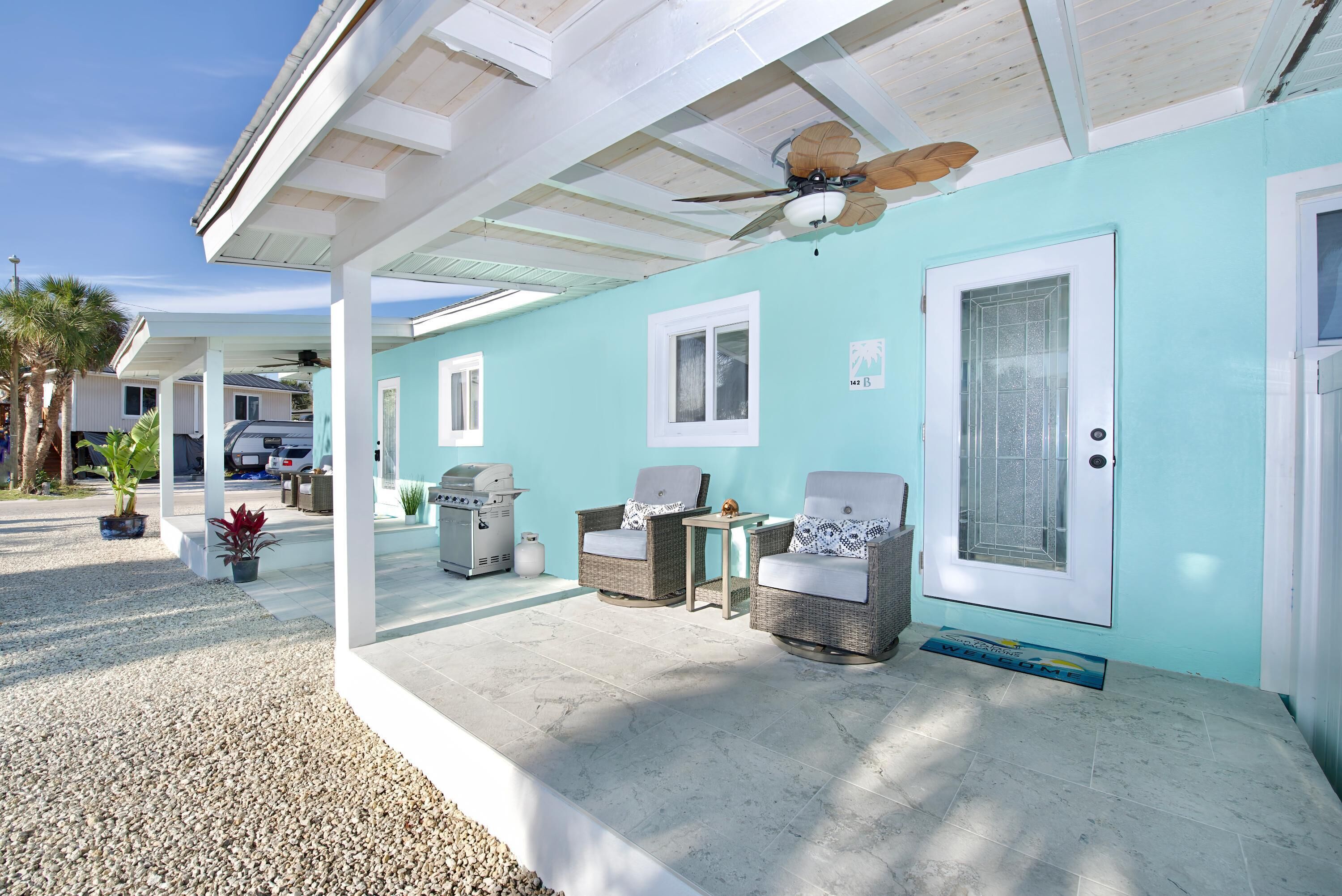 A covered outdoor area with two wicker chairs, a small table, and a ceiling fan.
