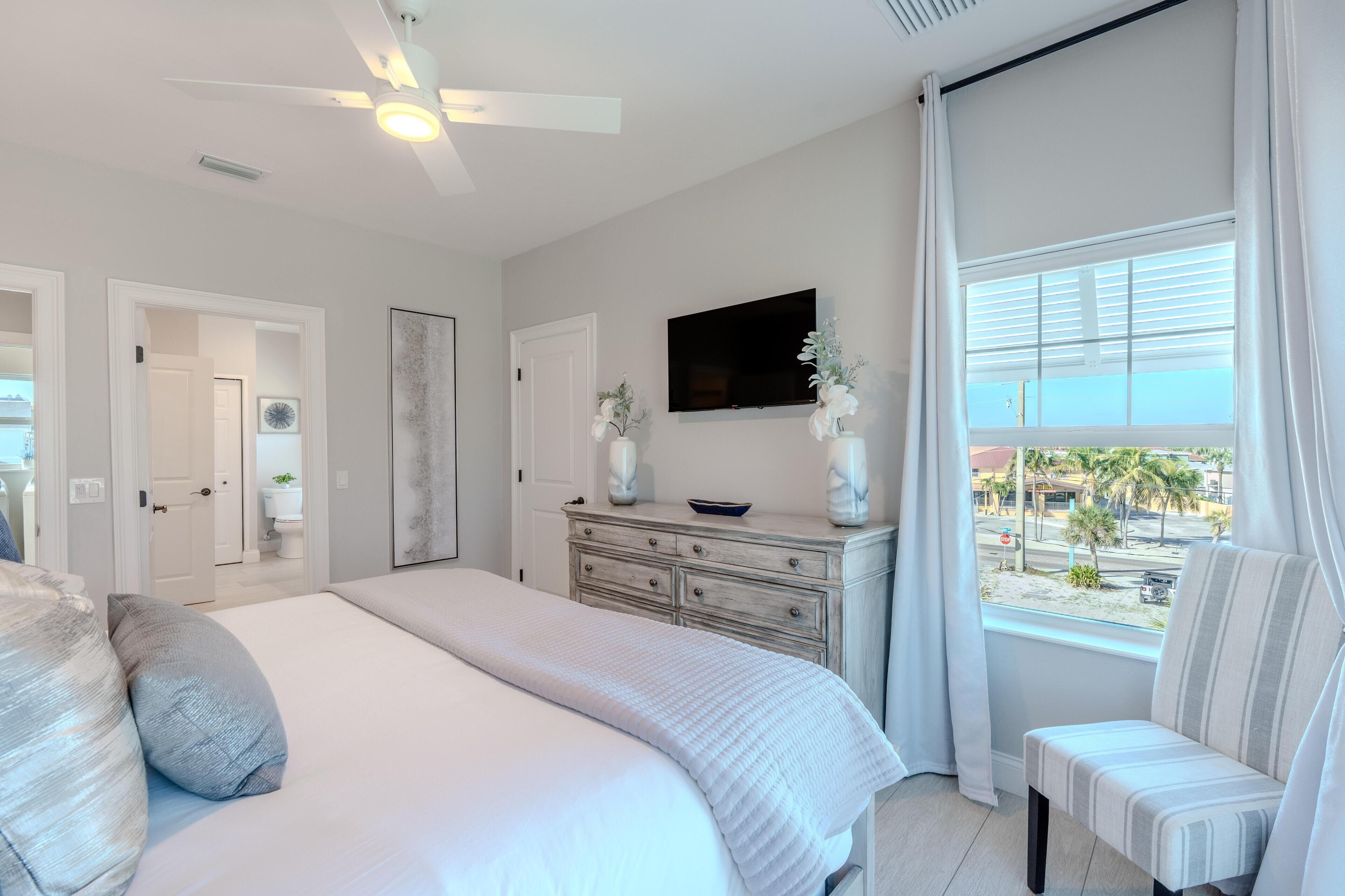 Quarto com cama, penteadeira, televisão e janela com cortinas.