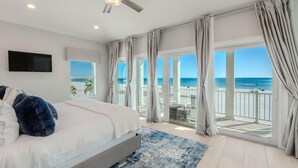 A bedroom with a large bed, a ceiling fan, a TV, and a view of the beach. - White Sugar Sands (Fort Myers Beach)