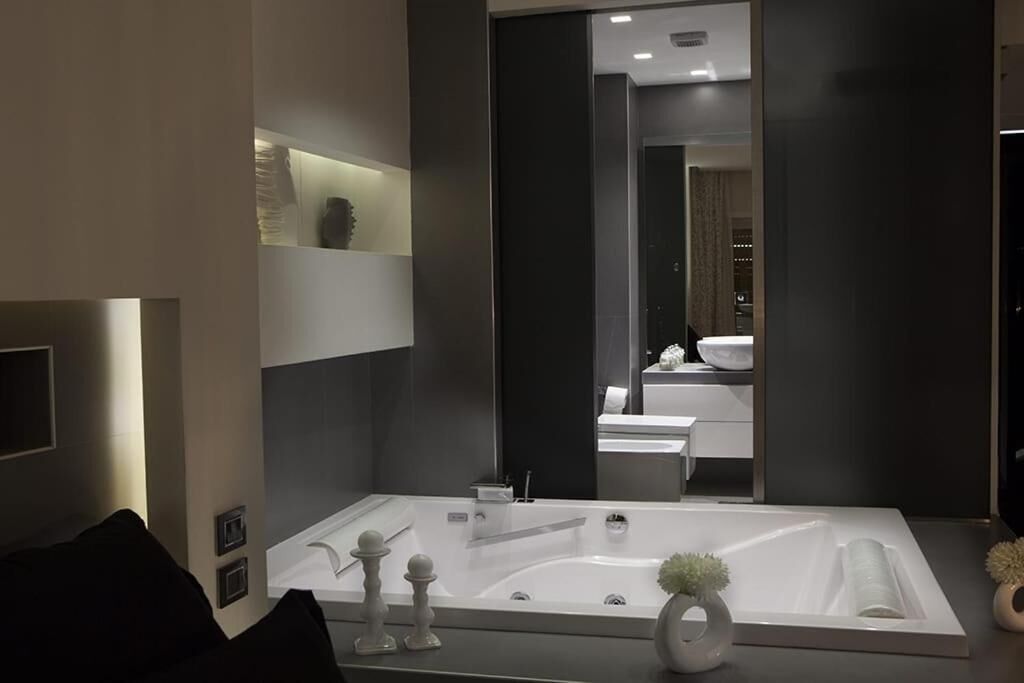 A modern bathroom with a large bathtub, a mirror, and a shelf with decorative items.
