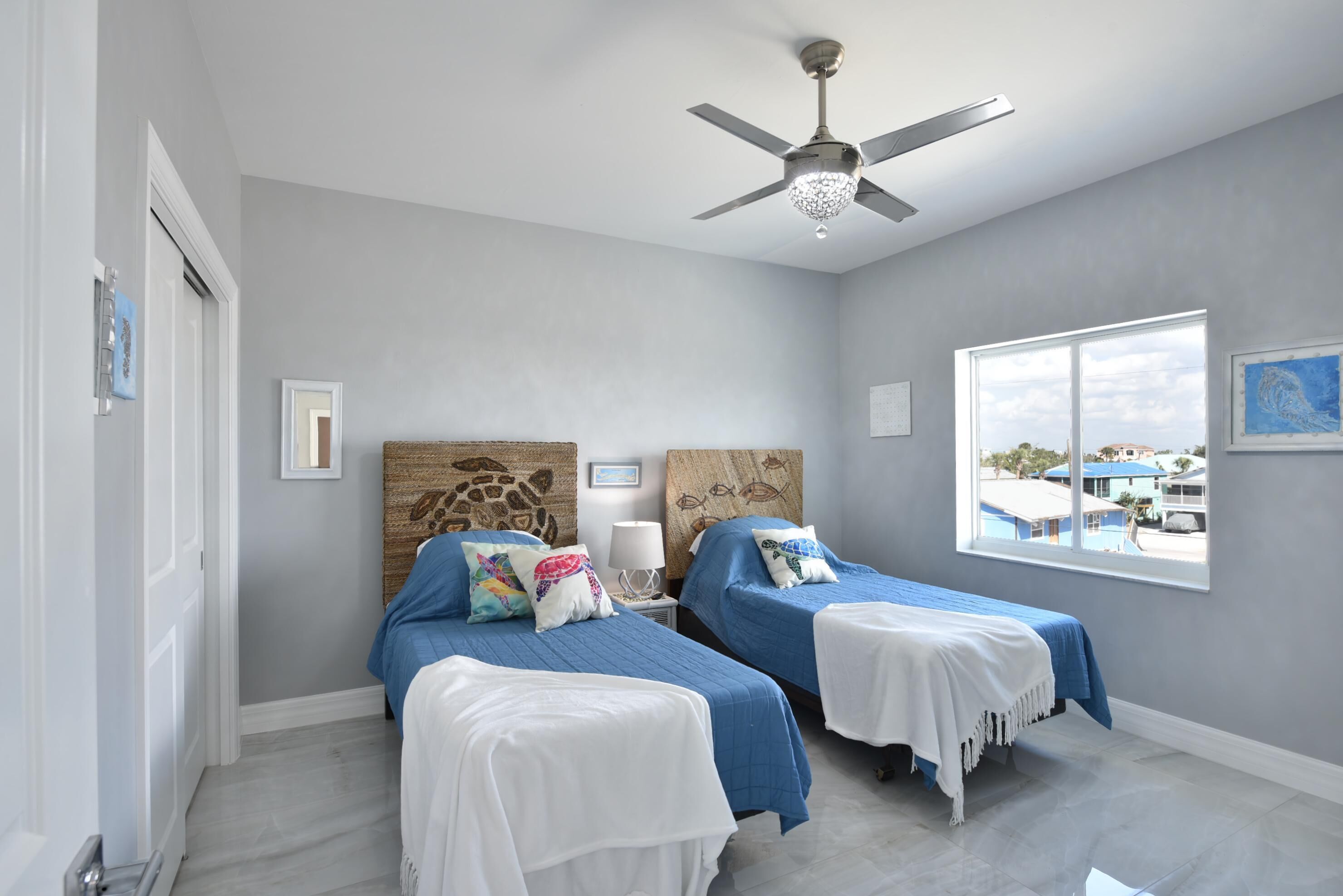 A bedroom with two beds, a ceiling fan, and a window with a view of buildings.