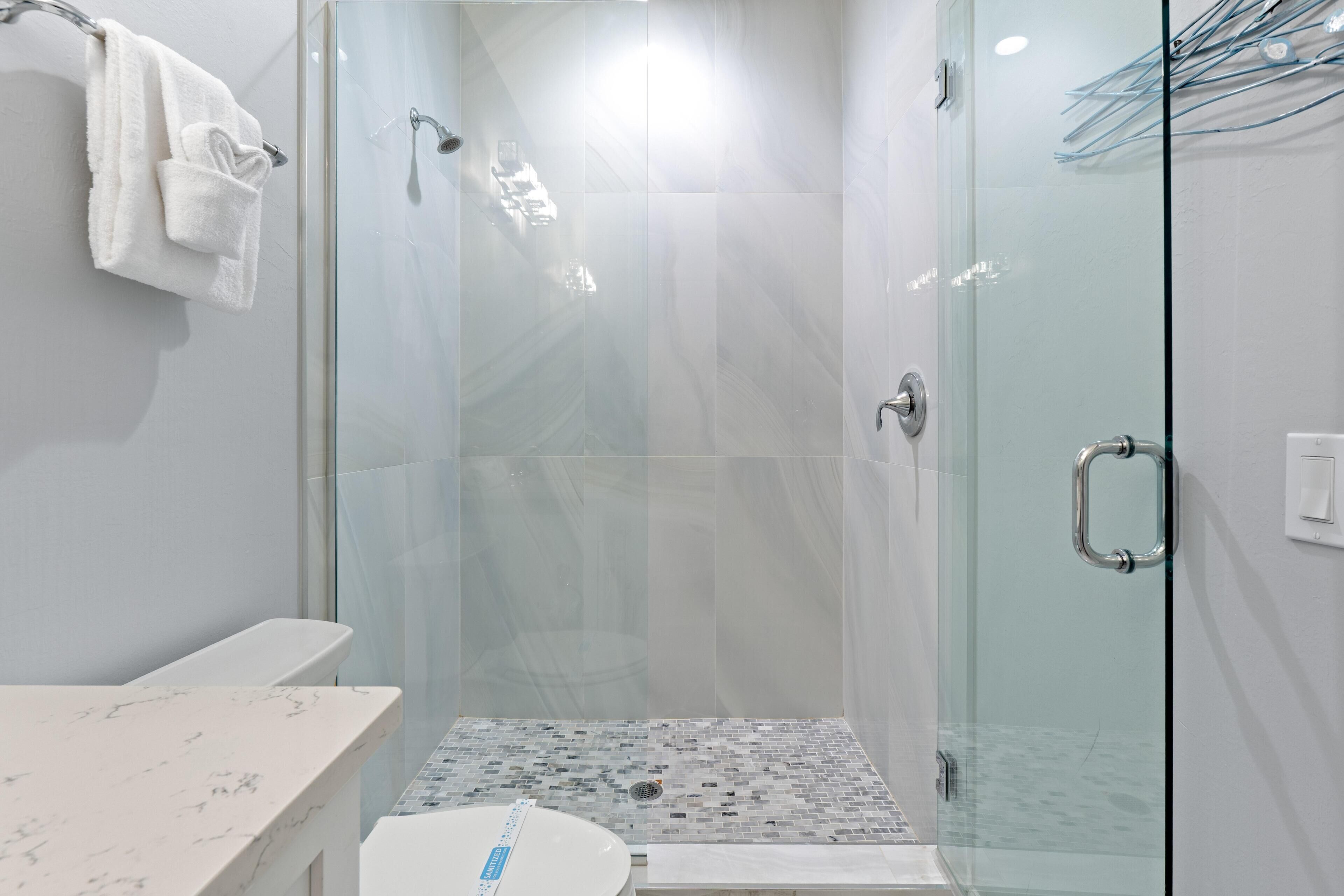 A modern bathroom with a glass shower enclosure, a marble-tiled shower floor, and a white toilet.