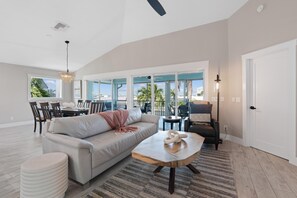 A spacious living room with a large sofa, a coffee table, and a dining area with chairs. - Harborside on Palermo (Fort Myers Beach)