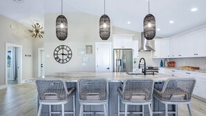 A modern kitchen with a large island, white cabinetry, and wicker bar stools. - Harborside on Palermo (Fort Myers Beach)