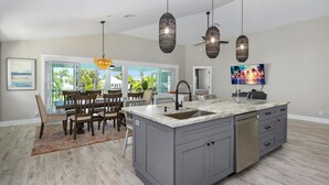A modern kitchen with a large island, grey cabinetry, and a dining area with wooden chairs and a table. - Harborside on Palermo (Fort Myers Beach)