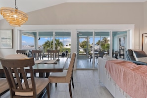 A spacious dining area with a large table and chairs, a view through glass doors to an outdoor patio, and a hanging light fixture. - Harborside on Palermo (Fort Myers Beach)