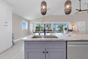 A kitchen with a large island, a dining area with outdoor views, and pendant lighting. - Harborside on Palermo (Fort Myers Beach)