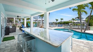 A poolside area with a bar, outdoor seating, and a view of the pool and surrounding landscape. - Harborside on Palermo (Fort Myers Beach)