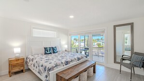 Une chambre avec un grand lit, un banc en bois, une table de chevet, une chaise et un balcon avec vue.