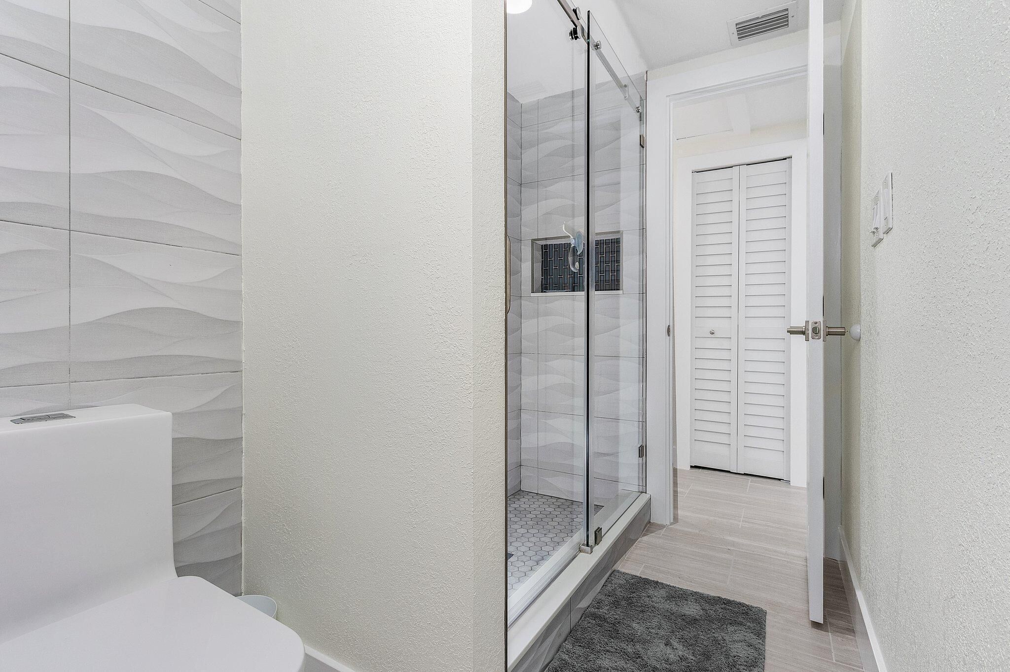 Ein modernes Badezimmer mit Duschkabine aus Glas, einer weißen Toilette und einer weißen Tür mit Klappläden.