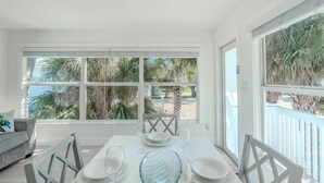 Un coin repas avec une table dressée pour quatre personnes, de grandes fenêtres et une vue sur des palmiers et une plage.
