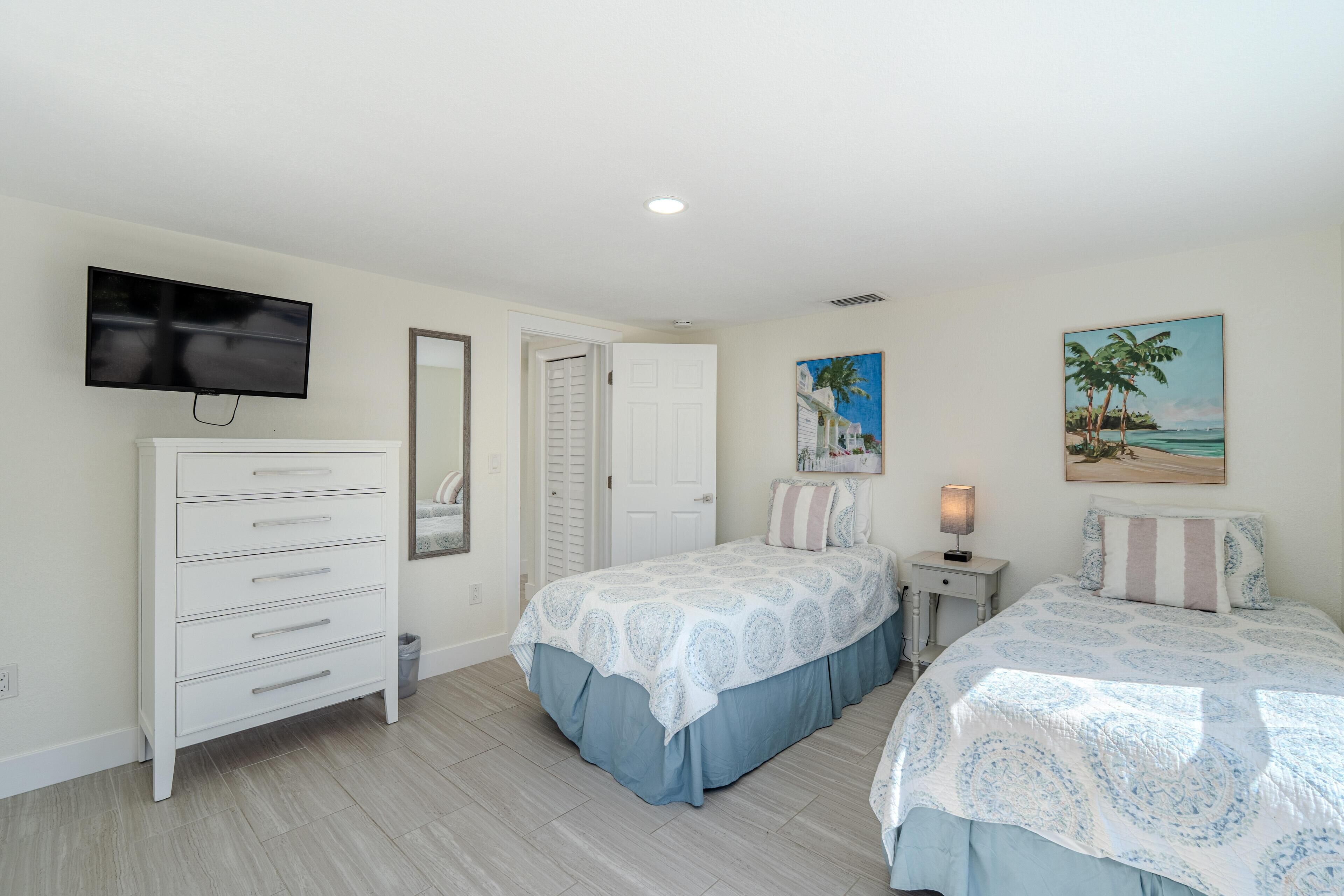 A bedroom with two beds, a dresser, a TV, and a painting of a beach scene.