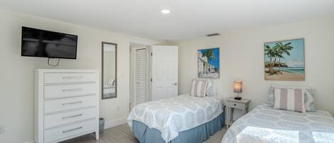 A bedroom with two beds, a dresser, a TV, and a painting of a beach scene.