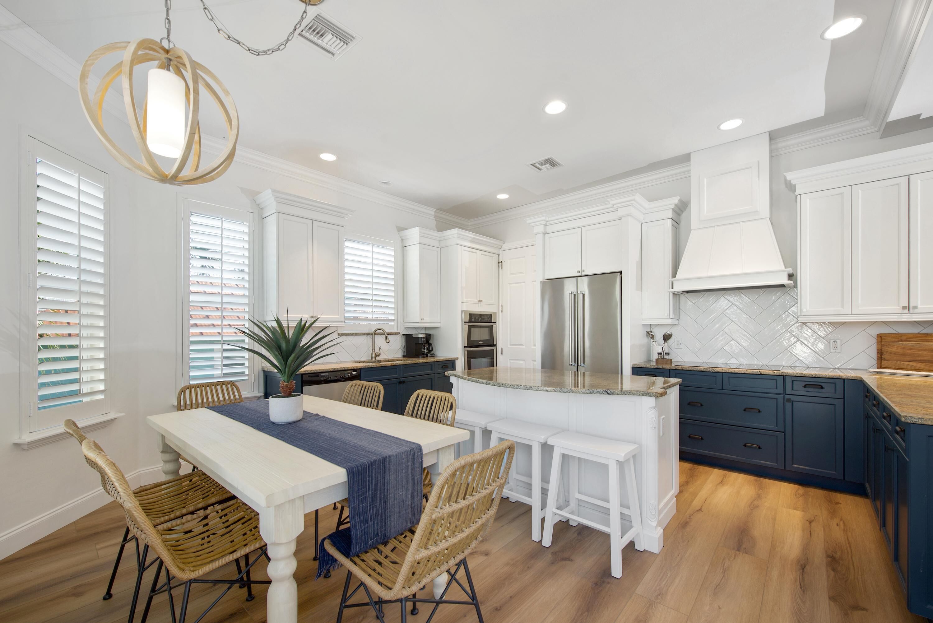 A modern kitchen with white cabinetry, a central island, and a dining area with wicker chairs.