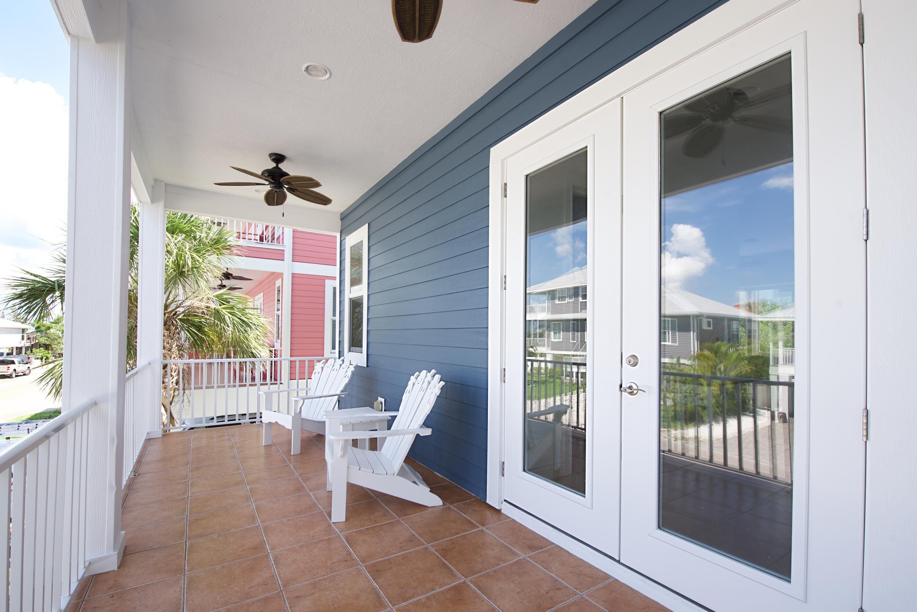 A covered porch with two white Adirondack chairs, a ceiling fan, and a sliding glass door.
