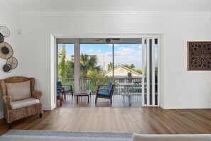 A room with a wicker sofa, a dining table with chairs, and a view through a sliding glass door to a balcony with a railing.
