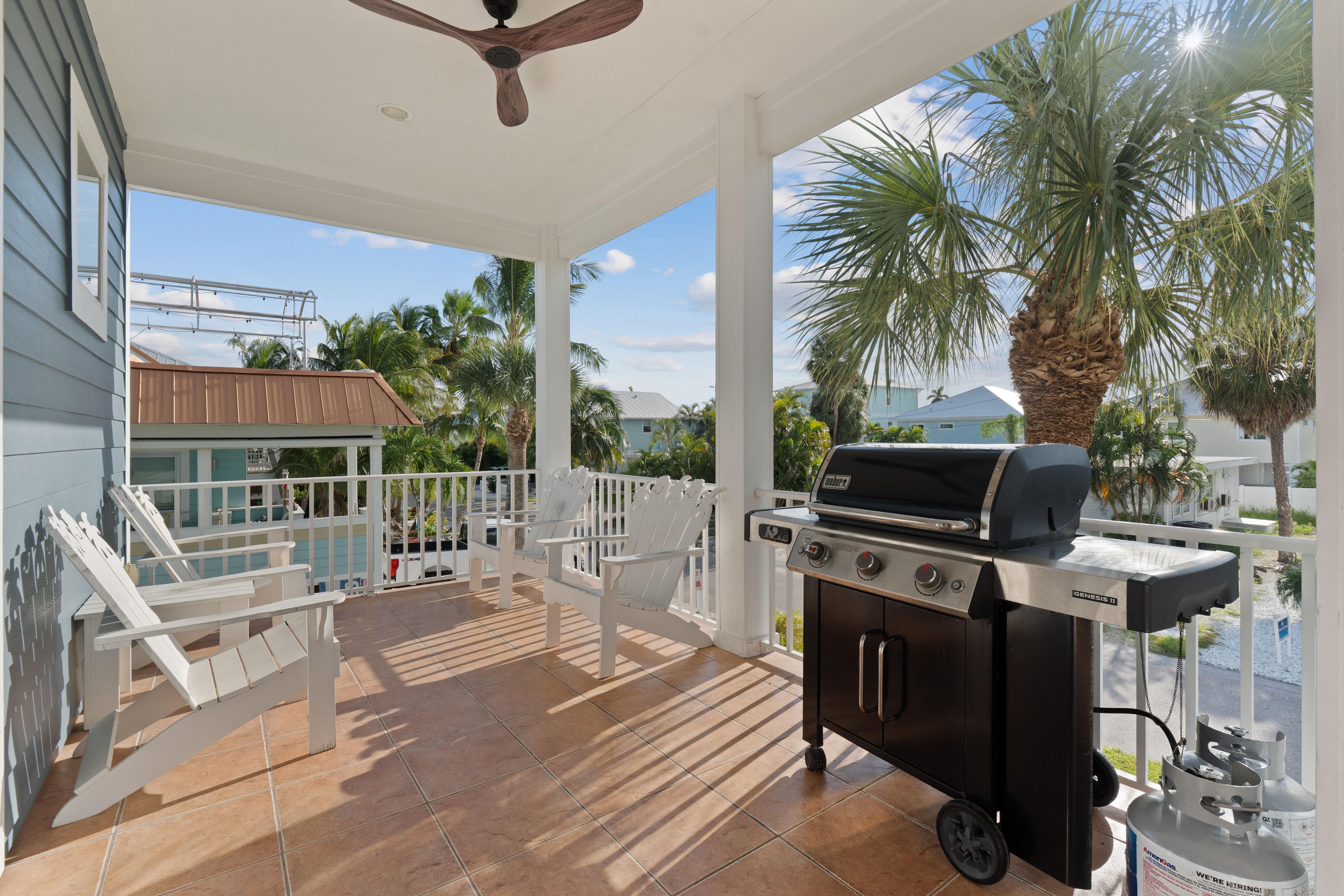 Ein überdachter Patio mit Grill, Gartenmöbeln und Blick auf Palmen und Häuser.