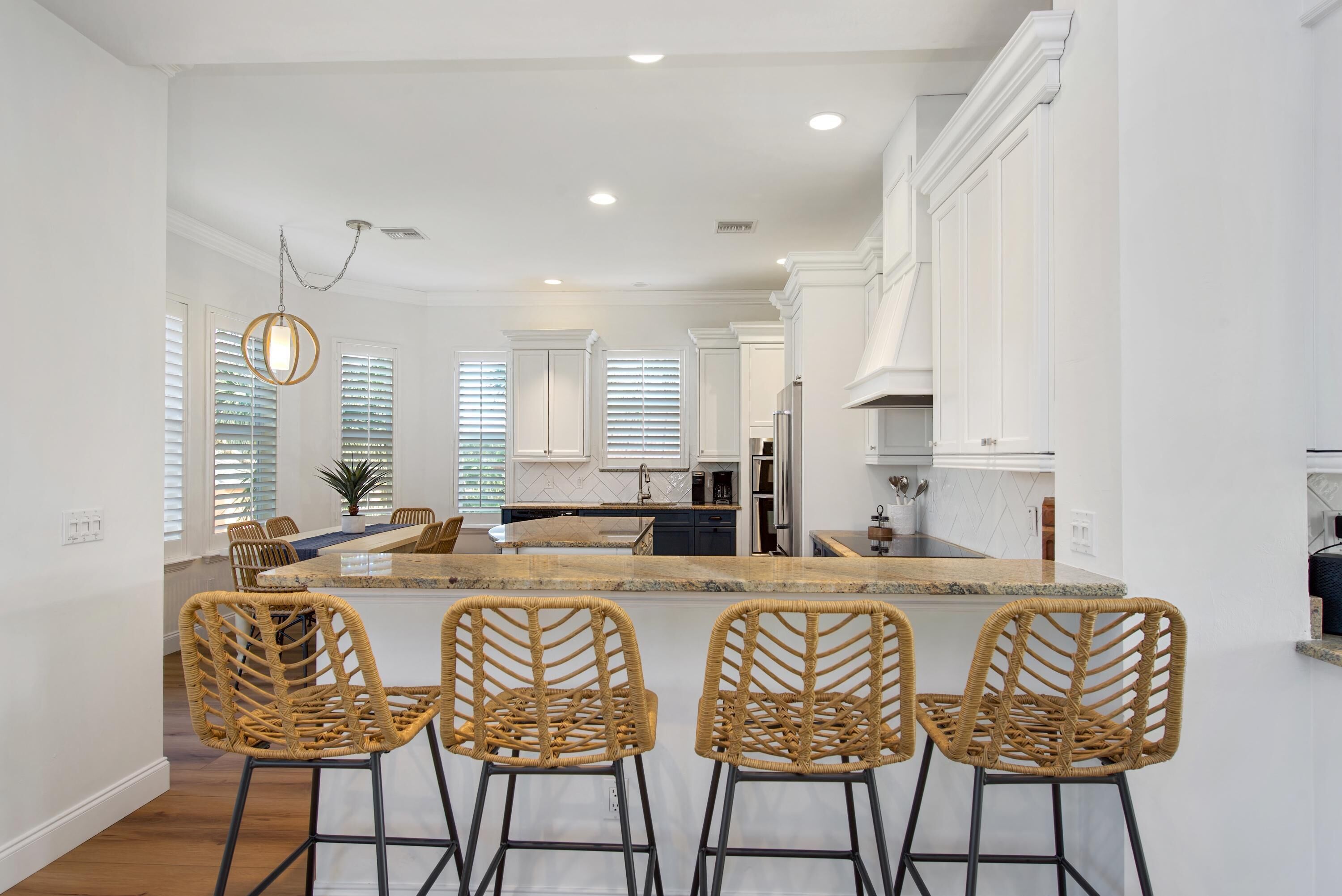 A modern kitchen with white cabinetry, a central island with bar stools, and a dining area with a table and chairs.