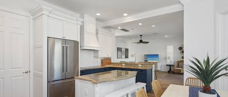 A kitchen with white cabinetry, a stainless steel refrigerator, a granite countertop island with bar stools, and a dining area with a table and chairs.