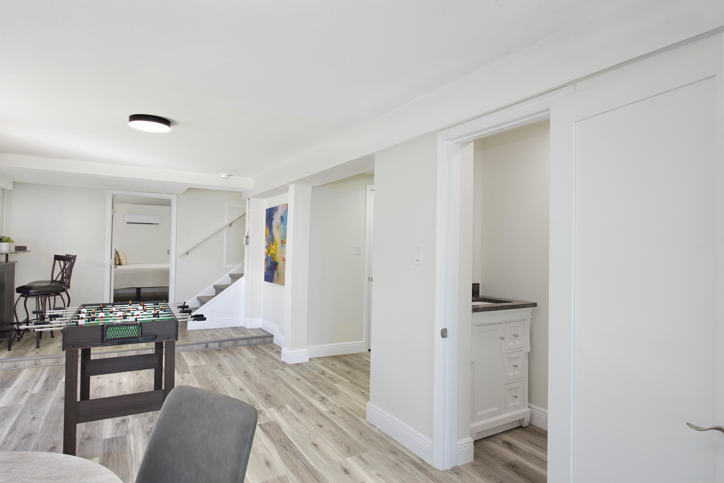 Uma sala de estar ampla com mesa de pebolim, mesa de jantar com cadeiras e escada para outro andar.