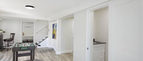 Uma sala de estar ampla com mesa de pebolim, mesa de jantar com cadeiras e escada para outro andar.