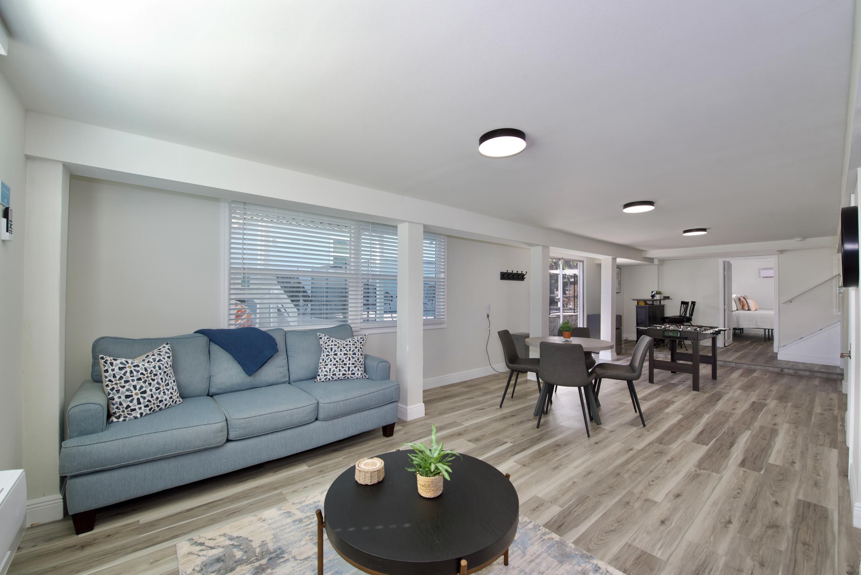 A modern living room with a grey sofa, a round black coffee table, and a dining area with a table and chairs.